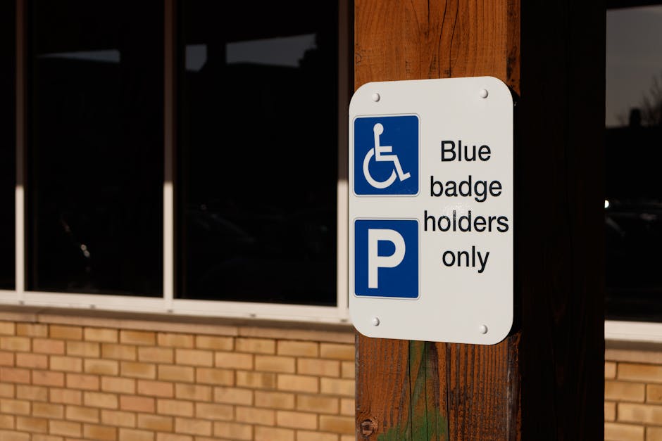 Close-up of a white rectangular parking sign attached to a wooden post outside a building. The sign displays a blue wheelchair symbol indicating accessibility, along with the text 'Blue badge holders